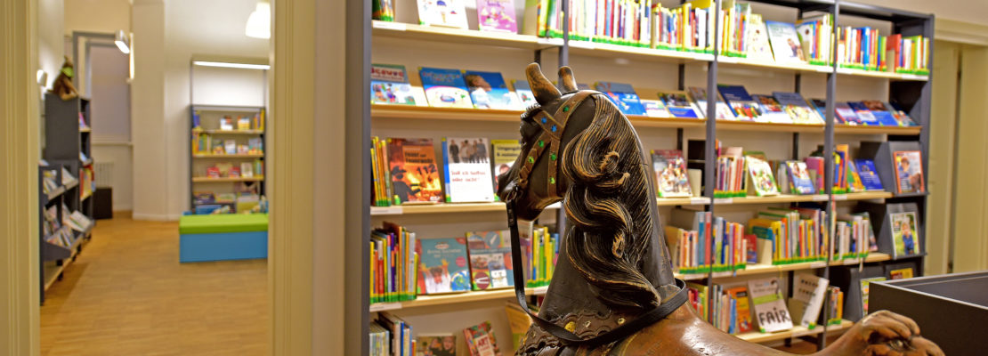 Pferdekarussell in Bibliothek Tolksdorf. Bücherregale im Hintergrund. Wissenswertes für Kinder.