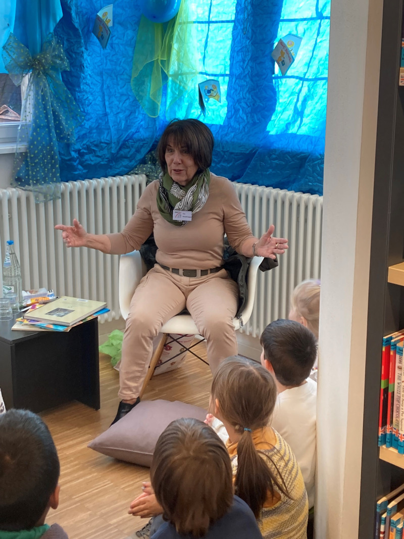 Frau liest Kindern in Bibliothek vor. Vorlese-Event mit Büchern und Zuhörern.